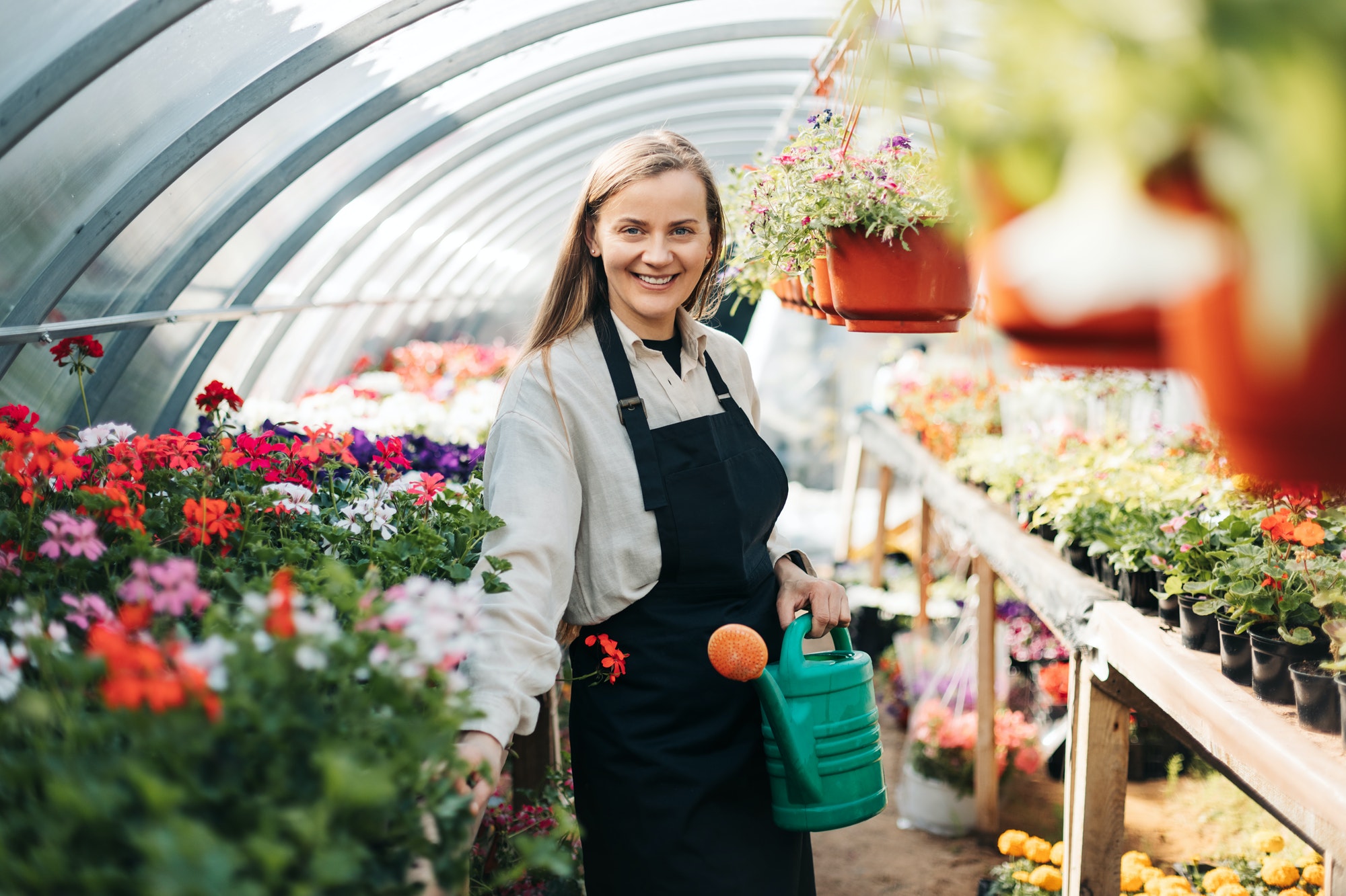 portrait of a young gardener woman watering flowers in a greenhouse daily care of plants